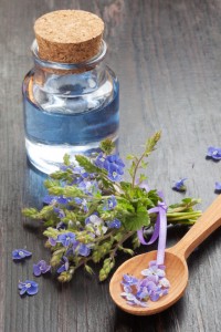 blue essential oil in glass bottle, wooden spoon and healing flo